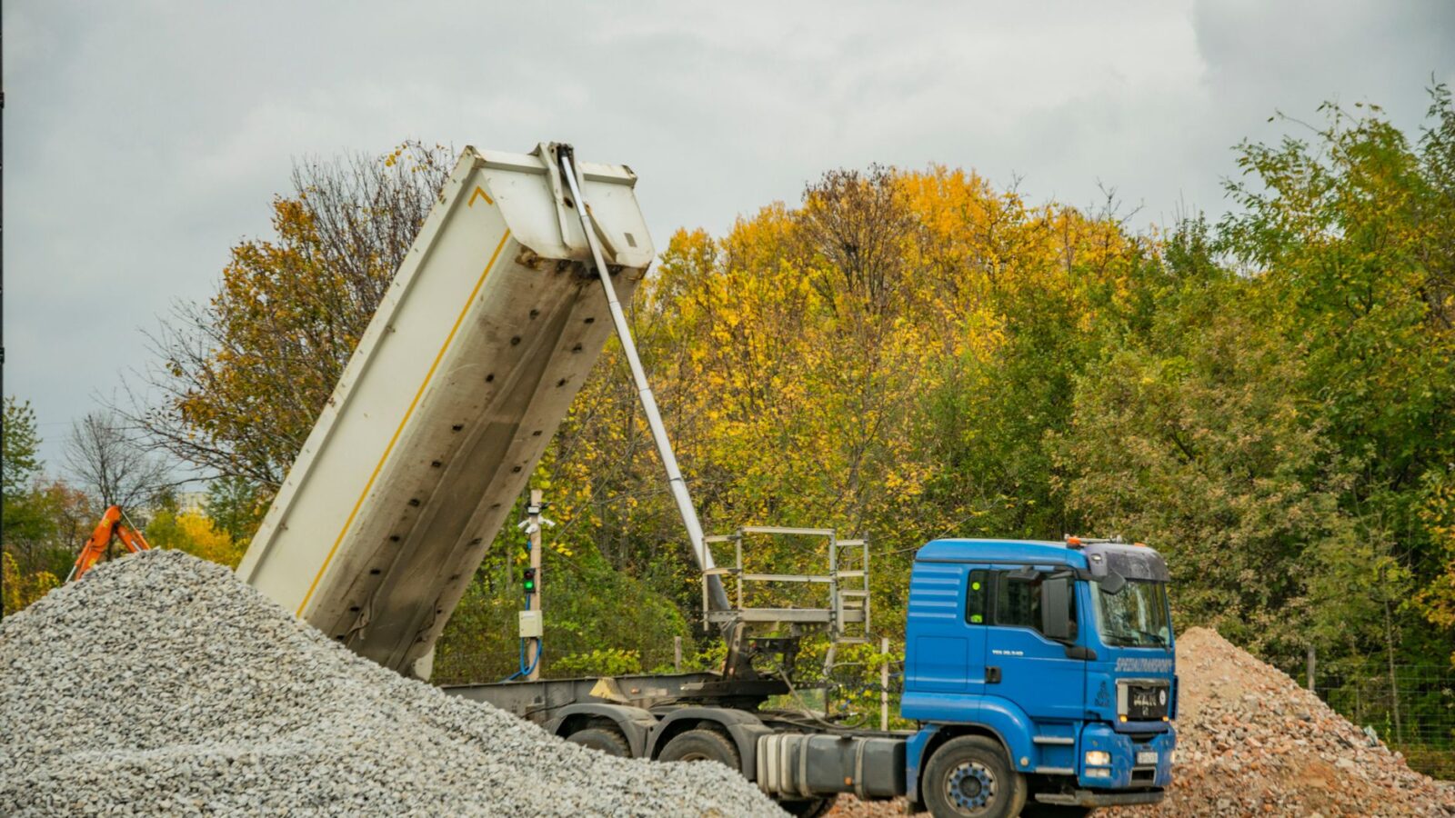A dump truck tipping a mounded pile of dark screened topsoil onto a gravel driveway beside a new raised bed frame.