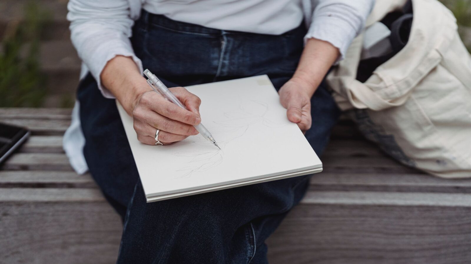 A weathered pocket notebook open on a garden bench beside pruning snips and a pencil, with tomato seedlings in the background.