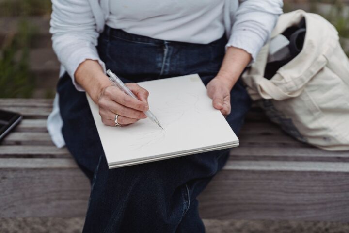A weathered pocket notebook open on a garden bench beside pruning snips and a pencil, with tomato seedlings in the background.
