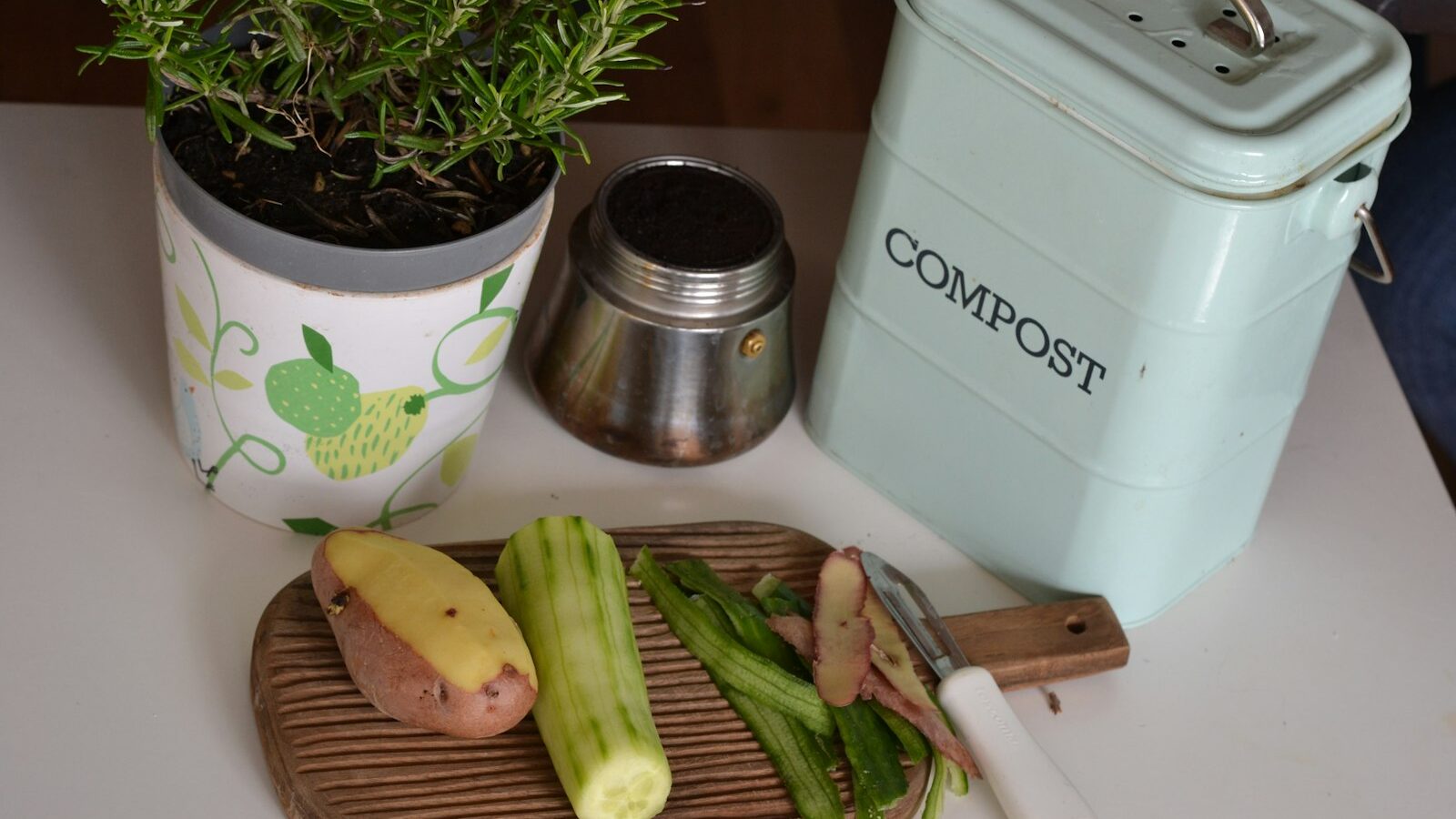 A stainless kitchen compost pail on a wooden counter holding fresh vegetable trimmings.