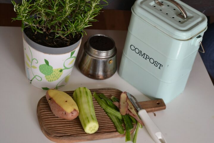 A stainless kitchen compost pail on a wooden counter holding fresh vegetable trimmings.