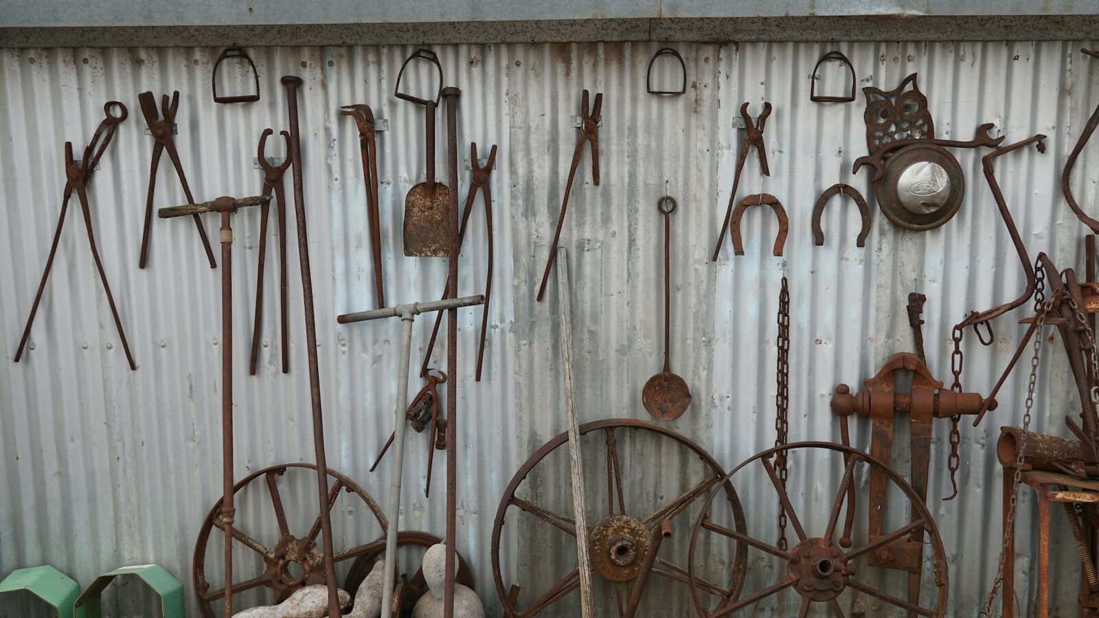 A tidy row of garden tools hanging on a shed wall, with a few unused implements standing in the corner.